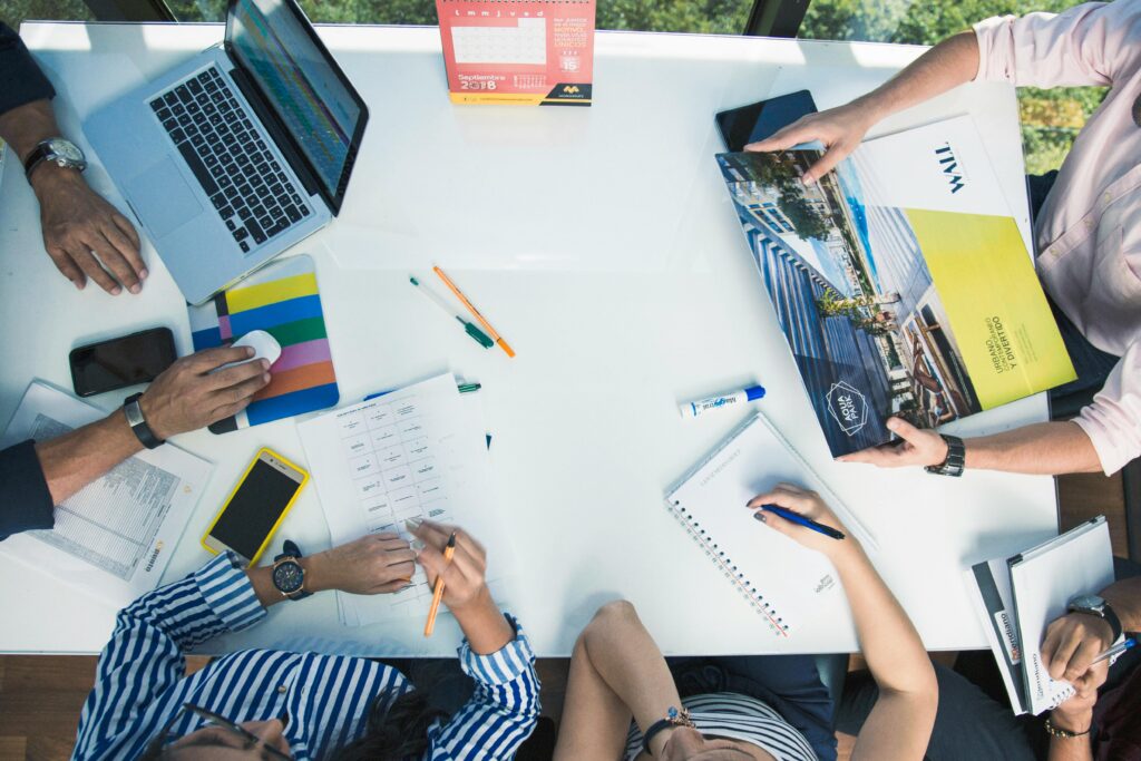From above of crop unrecognizable coworkers gathering around table with laptop and papers while working together in office